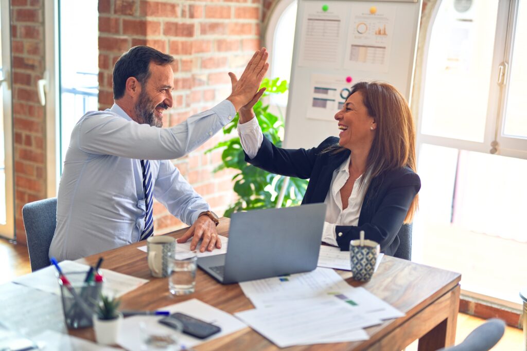 man and woman, in an office, smiling and giving each other a high 5