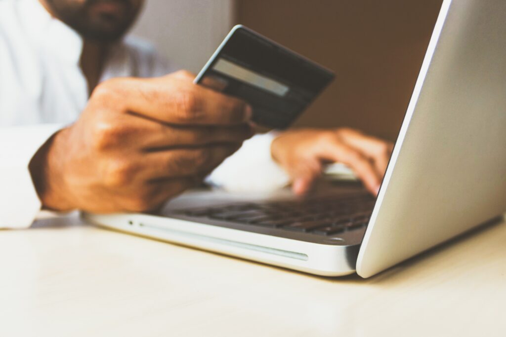 man holding a credit card in front of laptop screen for online shopping