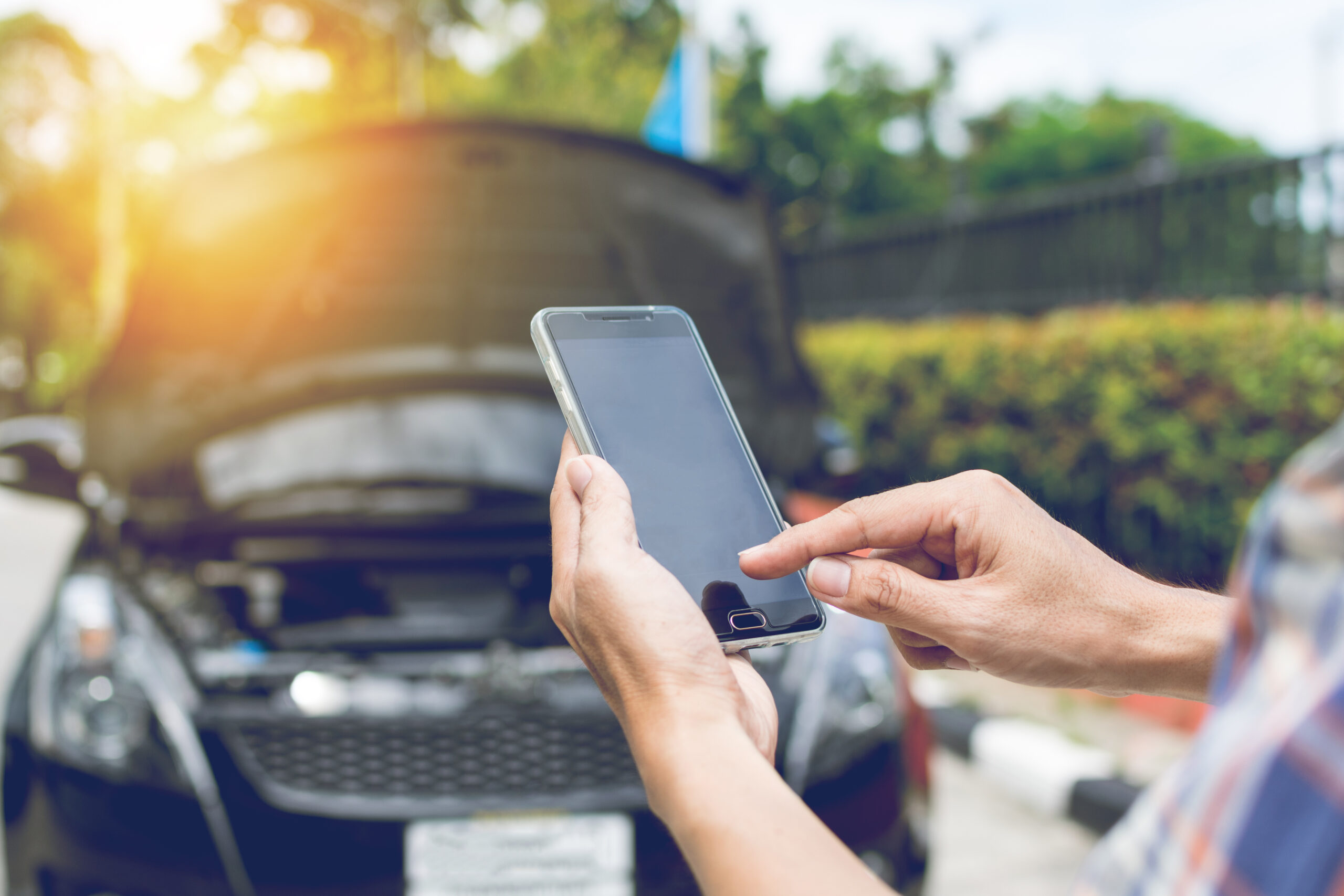 man using phone for urgent cash loan in front of broken down car